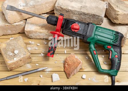 Hammer drill with a handle and old bricks on a wooden table. Selective focus. Stock Photo