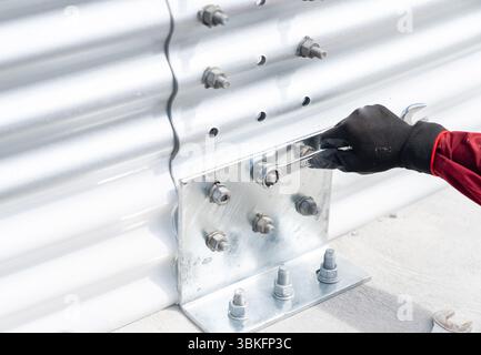 Tighten the bolts to secure the plate to the metal sheet wall using a wrench. Stock Photo