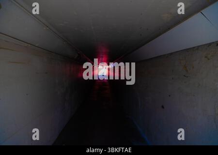 Long dark empty tunnel walkway with light at the end. Stock Photo