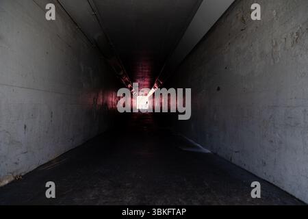 Long dark empty tunnel walkway with light at the end. Stock Photo