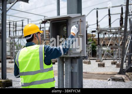 A power station engineer working on electrical control panel outdoors with safety helmet and vest Stock Photo