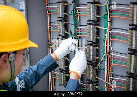 An engineer working carefully on wiring inside power station panel is focused on ensuring safety and functionality with precision and skill Stock Photo