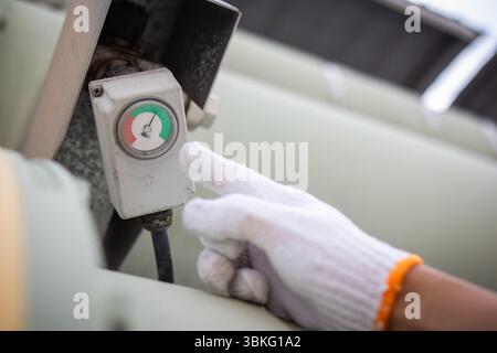 An engineer is working carefully to check power gauge at station wearing white glove showing focus and precision in industrial environment Stock Photo
