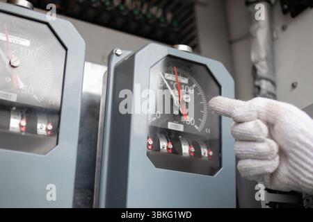 A temperature gauge inside substation shows power levels while wind outside affects transformer performance in this industrial setting Stock Photo