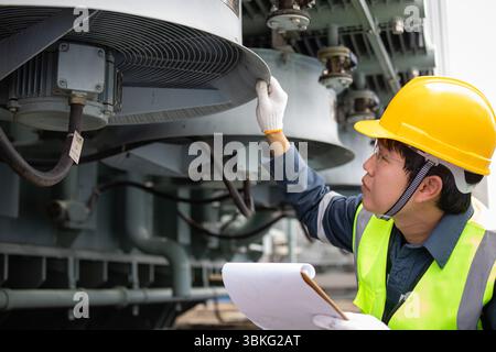 An inspection of transformer cooling system in substation is performed carefully by worker wearing safety helmet and vest to ensure proper function an Stock Photo