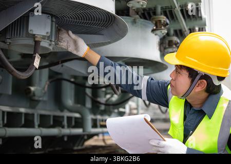 An engineer performs inspection on transformer cooling system at substation ensuring safety and efficiency with careful attention and protective gear Stock Photo