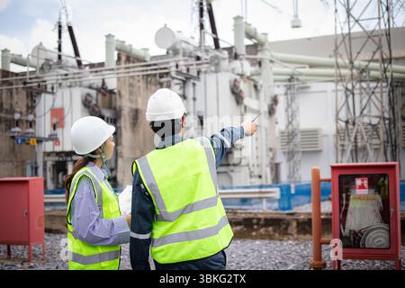 An engineer working at high voltage substation with safety helmet and reflective vest inspecting electrical equipment outdoors Stock Photo