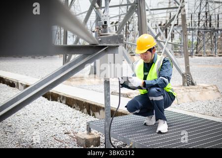 An engineer is working carefully at high voltage substation wearing safety gear and inspecting equipment to ensure proper operation and safety in indu Stock Photo