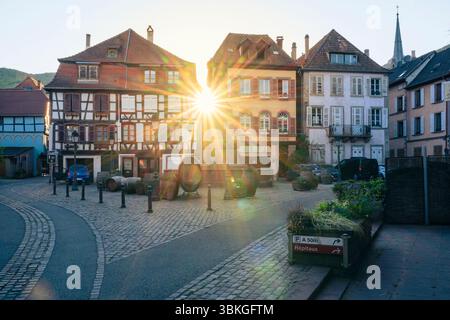 The setting sun shines between half-timbered houses on the Place de la Sinne with the Friedrich fountain in the old town centre of Ribeauvillé, Alsace Stock Photo