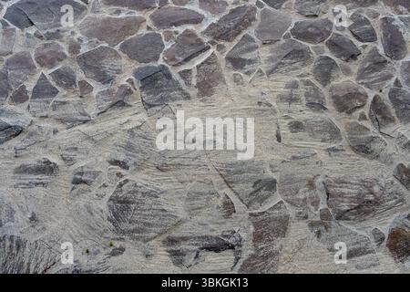 Stone path with a lot of texture and sands. The wall is made of stone and has a rough surface Stock Photo