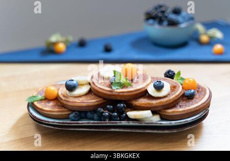 Blue plate pancakes on wood table and berries in background, warm daylight from above adds glow Stock Photo