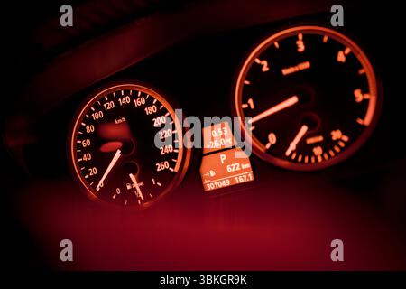 close up of an illuminated car dashboard displaying speed, rpm, temperature, and other information in a warm red glow Stock Photo