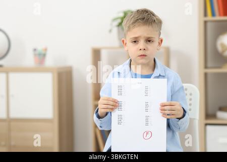 School grade. Sad boy holding answer sheet with letter F indoors, space for text Stock Photo
