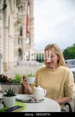 Woman enjoying tea at outdoor cafe near historic European building facade Stock Photo