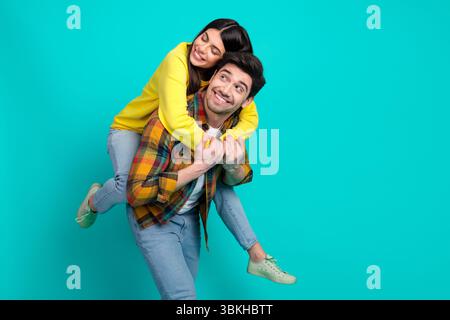 Joyful young couple having fun on turquoise background piggybacking and laughing during leisure time together Stock Photo