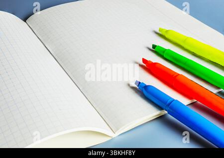 A close-up image of four colorful highlighters (yellow, green, orange, and blue) placed diagonally on an open grid notebook. Stock Photo