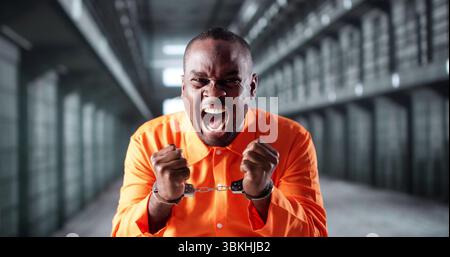 Incarcerated African American Man In Orange Uniform Standing By Bars. Stock Photo