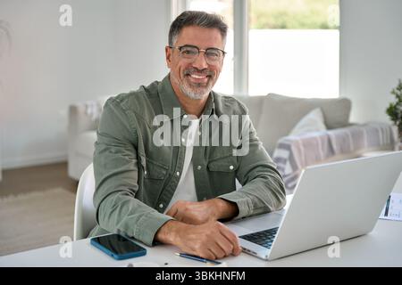 Happy middle aged man using laptop computer at home table. Portrait Stock Photo