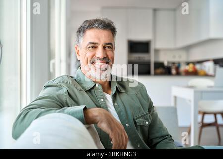 Portrait of happy middle aged man sitting on couch at home looking at camera. Stock Photo