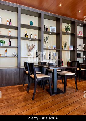 A stylish restaurant interior in Germany, featuring wooden flooring, dark wood shelves with decorative items and bottles, and a clean dining setup. Stock Photo