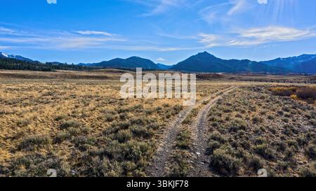 Sawtooth National Forest, Idaho, USA - October 16th 2020: A dirt road cuts through a grassy field, leading towards the mountains in the distance. Stock Photo