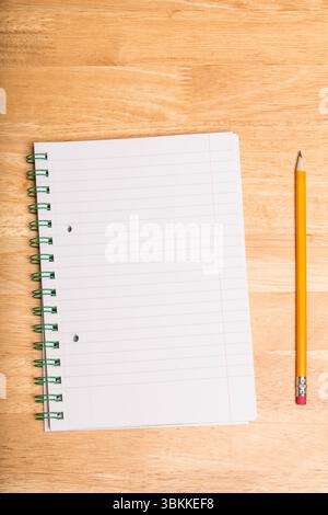 Spiral-bound lined notebook is lying open on wooden tabletop, with yellow pencil resting parallel Stock Photo
