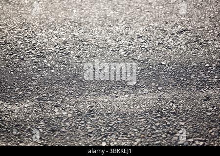 Close-up flat design showing rough asphalt pavement surface with stones reflecting subtle light Stock Photo