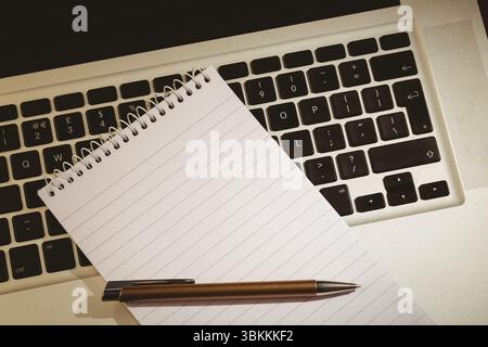 spiral-bound notebook and metallic pen are resting diagonally on laptop keyboard in flat design Stock Photo