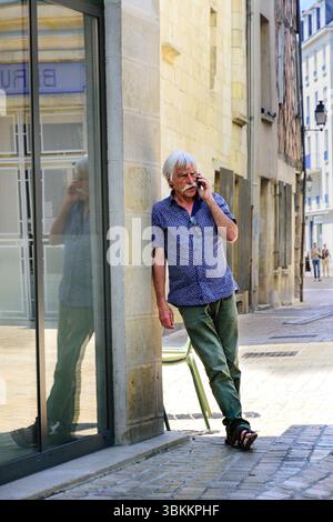 Middle-aged man talking on mobile phone whilst leaning on corner of building - central France. Stock Photo