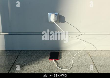 a red iPhone charging from a wall socket with EU adapter from british plug Stock Photo