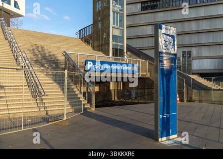 Entrance to Jaarbeursplein bicycle parking in Utrecht, Netherlands, with blue signage, stairs, and modern urban architecture in evening sunlight. Utre Stock Photo