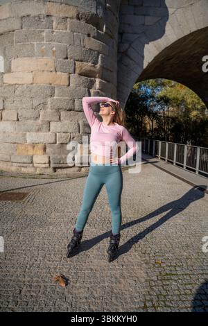 Young sporty woman posing with inline skates under a bridge during a sunny day Stock Photo