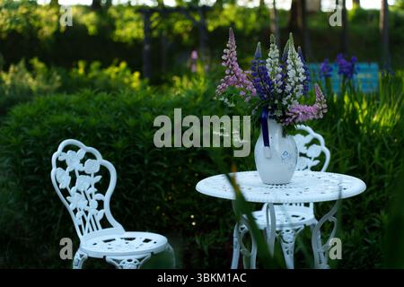 White garden furniture with flowers on the table in a green garden setting. Stock Photo