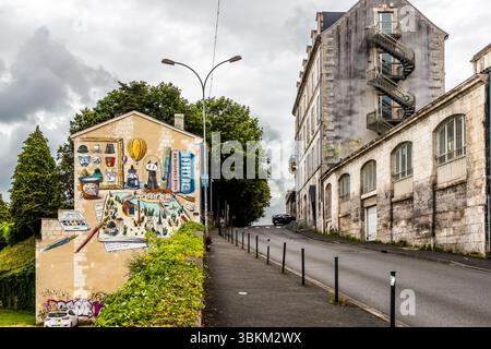 Building with a colourful mural depicting various elements representing the city of Angoulême. On the right is an older building with a spiral staircase. Angoulême is recognized as a UNESCO Creative City in the category of literature since 2019 Rue de Bordeaux, Angoulême, Nouvelle-Aquitaine, France Stock Photo