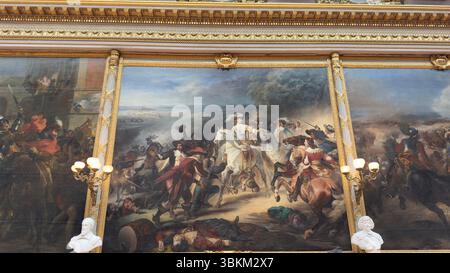 Image shows three framed battle paintings in a gilded hall, illuminated by a chandelier. Busts are placed at the bottom of the painting. Stock Photo