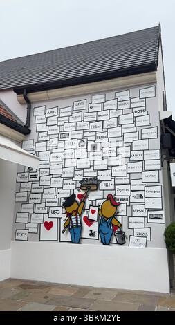 Building exterior featuring brand logos on a wall with cartoon characters applying them, and a tiled walkway. Stock Photo