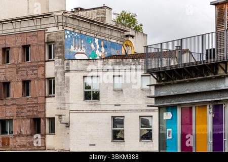 Building façades on the Place du Champ de Mars in Angoulême: on the roof of one of the buildings, a large-scale mural featuring characters from the Franco-Belgian comic tradition; coloured door elements can be seen on the right-hand edge of the picture. Angoulême hosts the Festival International de la Bande Dessinée, the most important international comic festival, and incorporates bande dessinée culture into the cityscape in many ways. Angoulême is recognized as a UNESCO Creative City in the category of literature since 2019. Place du Champ de Mars, Angoulême, Charente, Nouvelle-Aquitaine, Fr Stock Photo