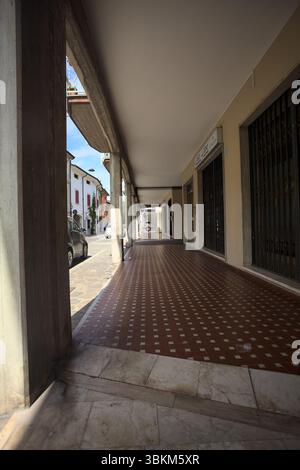Modern porch under a building with shops closed by metallic shutters by the edge of a street on a sunny day Stock Photo