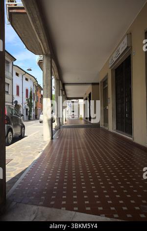 Modern porch under a building with shops closed by metallic shutters by the edge of a street on a sunny day Stock Photo