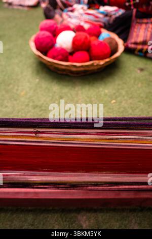 A bowl of colorful yarn balls sits on a green surface with a bundle of threads in the foreground. Stock Photo