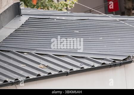 This image shows a damaged corrugated metal roof on a gray building, likely after a storm. repair is needed due to visible bends and missing fasteners Stock Photo