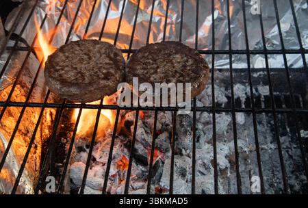 Two juicy burgers sizzling on a barbecue grill, cooking over hot coals for a classic outdoor barbecue experience. Stock Photo