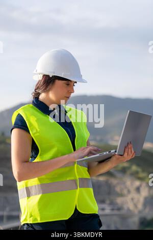 Female engineer using laptop managing civil engineering infrastructure project Stock Photo