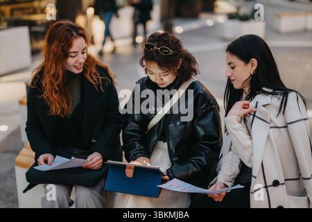 Group of young women collaborating and reviewing documents in urban outdoor setting Stock Photo