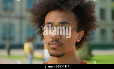 Portrait young male student man African American guy serious calm confident face wearing glasses looking at camera outdoors near university campus Stock Photo