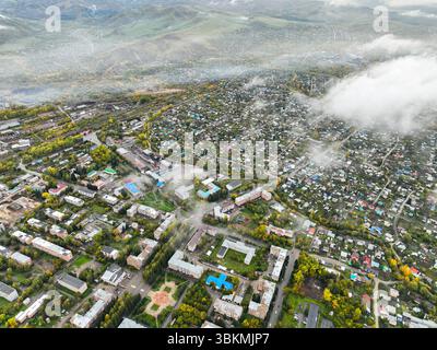 An aerial view of the urban area of Ridder, Kazakhstan, with residential buildings and autumn trees partially obscured by low-lying mist and clouds Stock Photo