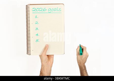 2026 goals written by green marker on a notebook held by a man. Isolated on white background. Stock Photo