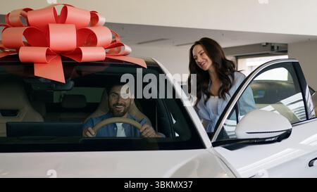 Happy Caucasian family buying new car electric automobile choosing decision carefree talking man sitting inside auto trying test drive discuss with Stock Photo