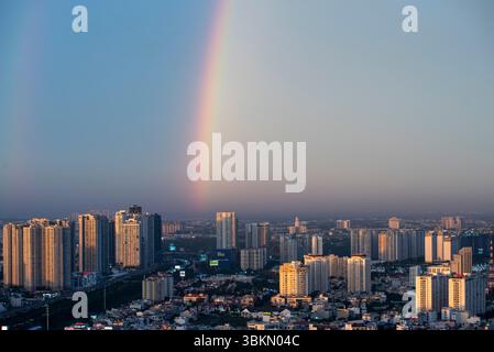 Rainbow is seen in the sky above a city. The rainbow is long and spans from the left side of the image to the right side Stock Photo