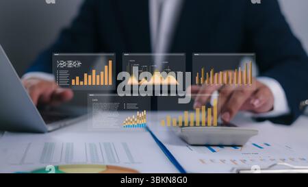 Businessman calculates financial data using a calculator and laptop on a desk filled with charts and reports. Ideal for illustrating accounting, budge Stock Photo